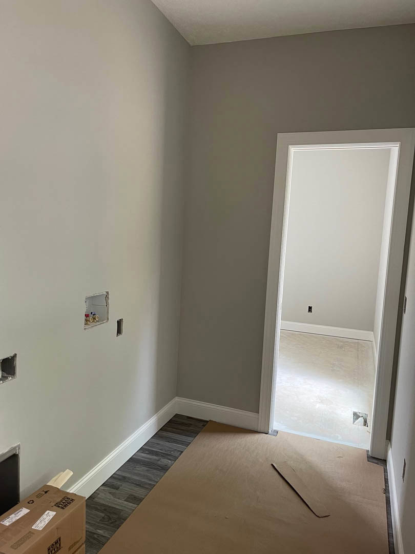 Wood laminate flooring with a brown cardboard box and white labels near an open doorway, white plaster wall featuring a small hole.