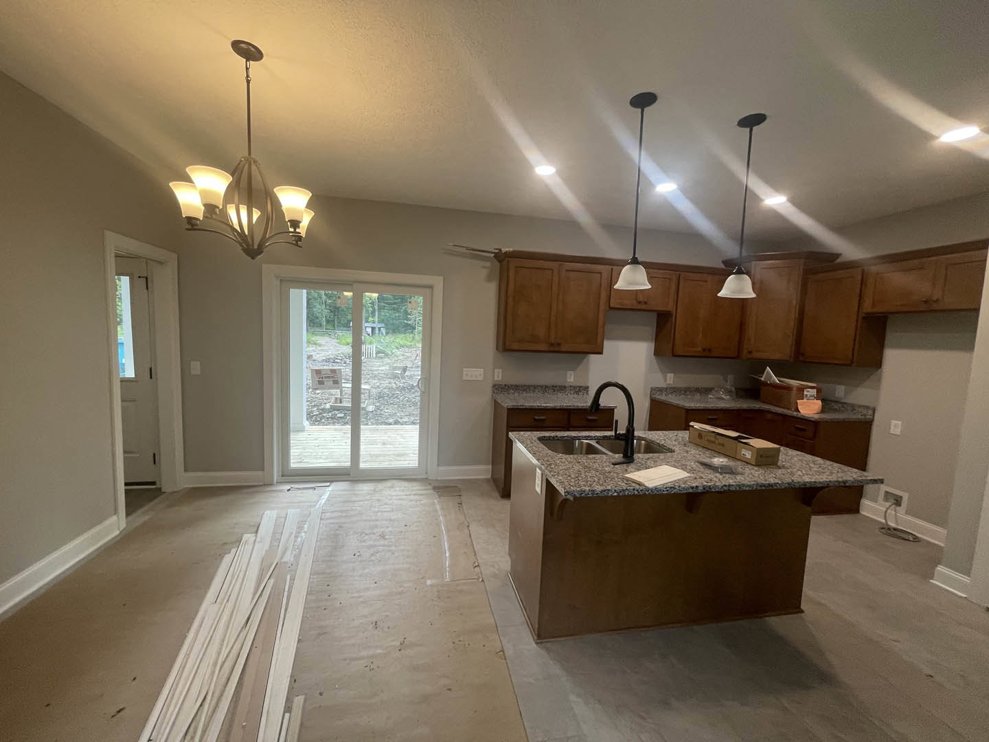 Open kitchen with white cabinetry, stainless steel sink set in a light stone countertop, sliding glass door overlooking green yard, modern chandelier above, hardwood flooring, and