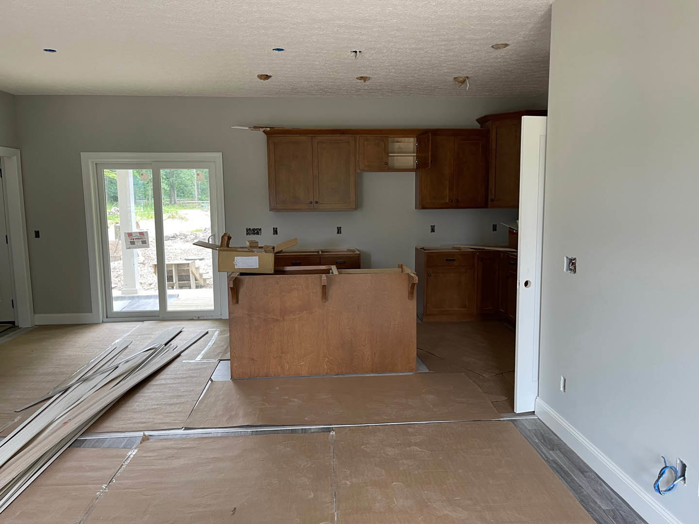 Kitchen with natural wood cabinets, matching wood plank flooring, light-colored countertops, stainless steel sink, and neutral tile backsplash.
