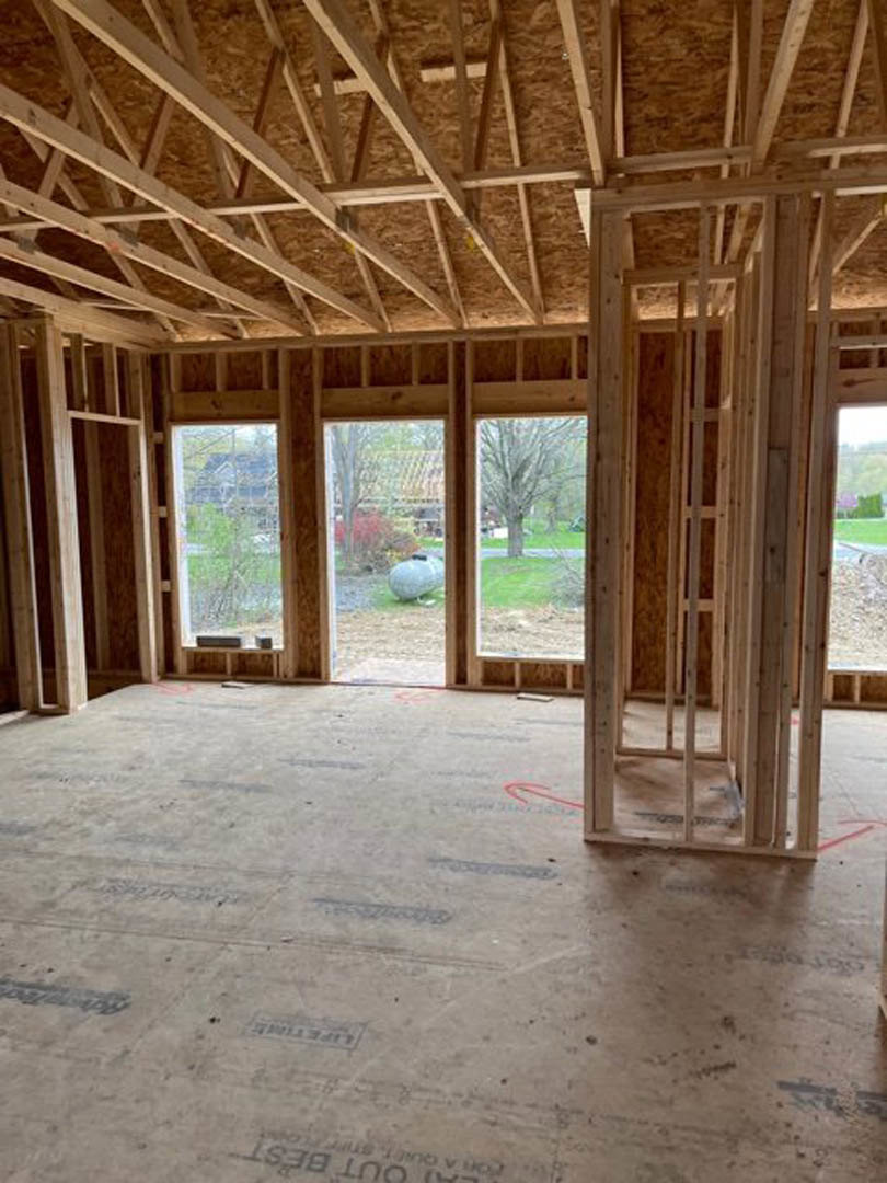 Unfinished room with exposed wooden beams, framed window, and construction materials on subfloor