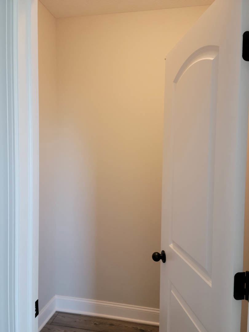 White paneled door with matte black round knobs, set against smooth white plaster wall and light wood flooring, simple baseboard molding visible