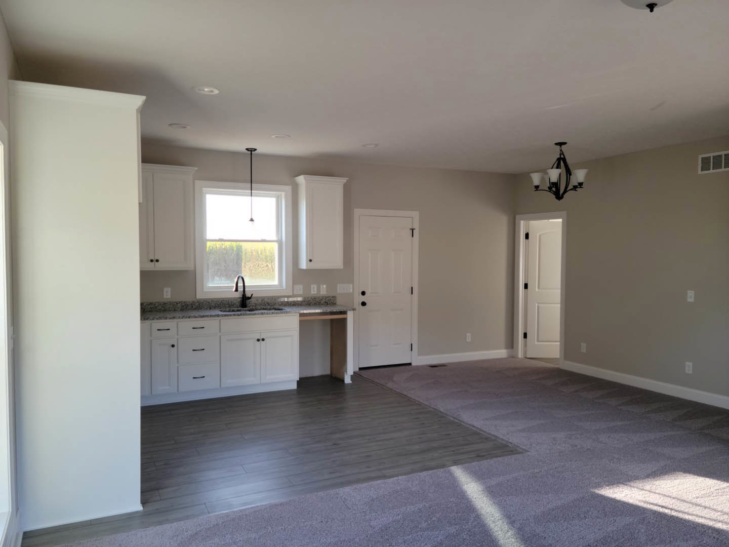 Kitchen with white cabinetry, black hardware, tile backsplash, stainless steel sink beneath a window, light wood flooring, and a modern chandelier.