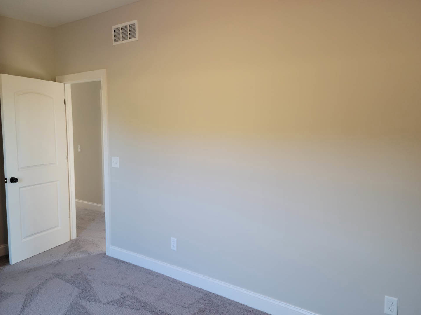 Open white door with black knob, white plaster walls, light switch, electrical outlet, floor vent, wood flooring, and white baseboard molding