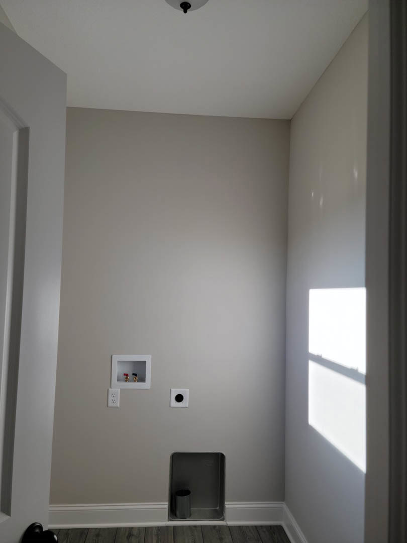 White plaster wall with a square recessed shelf, electrical outlet, and a white-framed fixture featuring red and blue faucet handles; black box and metal container with black pipe