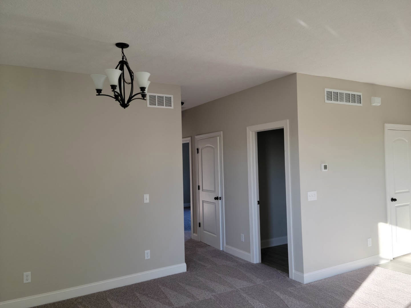 Chandelier hanging from white ceiling in a room with light plaster walls, two white doors with black knobs, and wood flooring