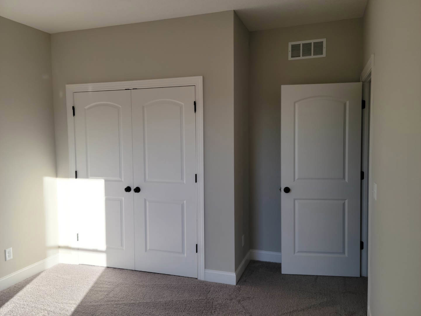Carpeted room featuring a white double door with black knobs, single white door with black knob, wall vent, and white walls