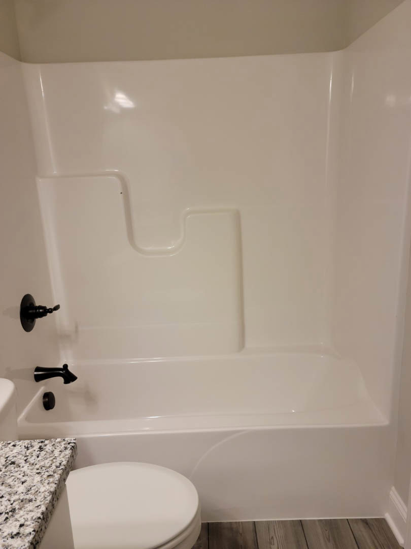 White freestanding bathtub and modern toilet on light tile floor, white sink with chrome faucet, wood countertop, close-up of toilet seat, black faucet, neutral bathroom walls.