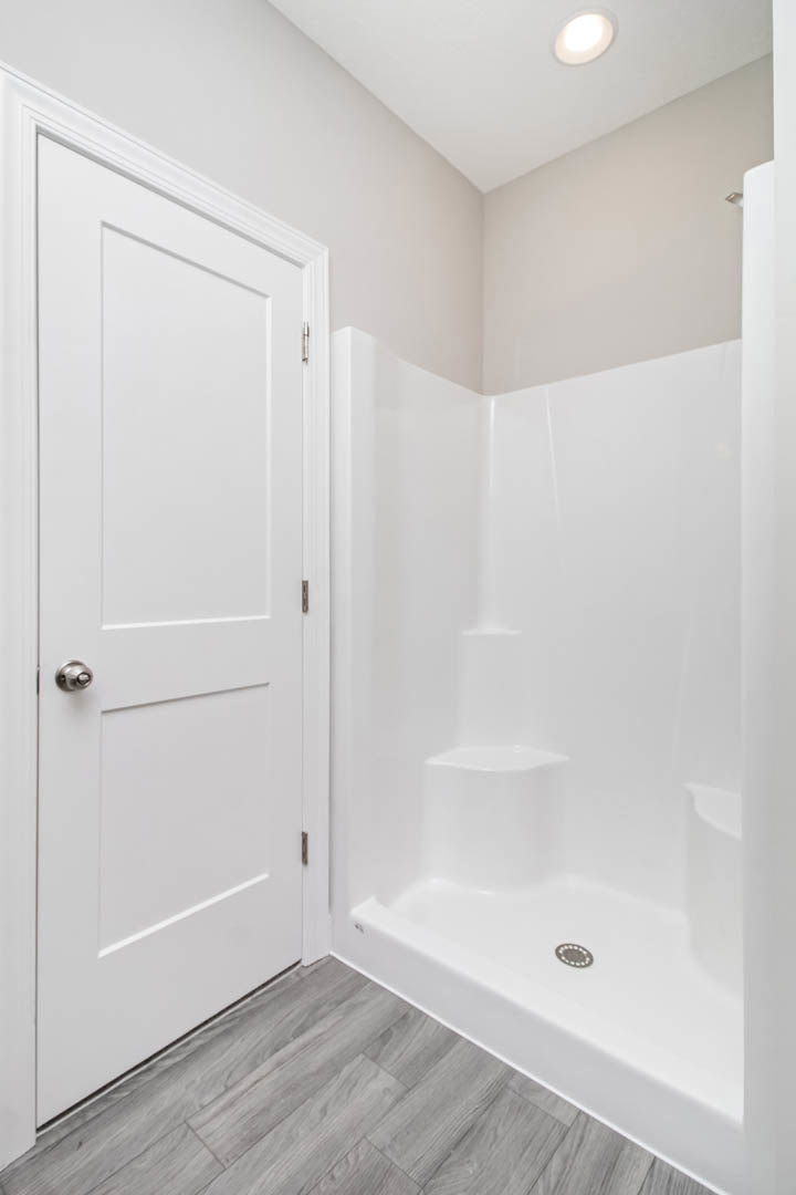 White tile shower with built-in drain, white paneled door, wood floor, recessed ceiling light