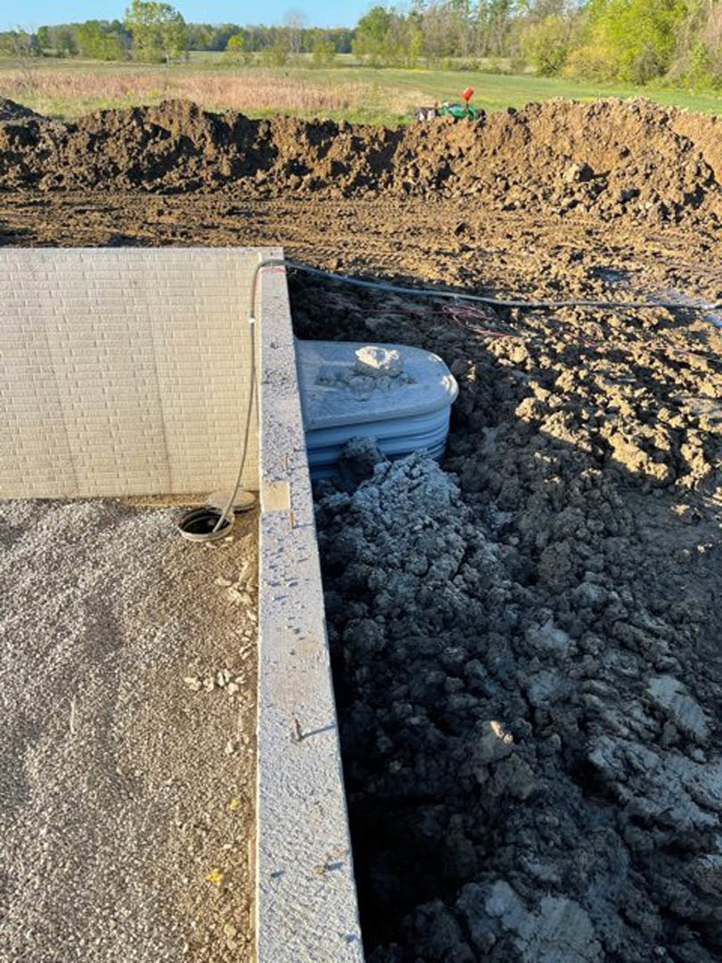Concrete wall with exposed pipe and adjacent pile of dirt on outdoor ground