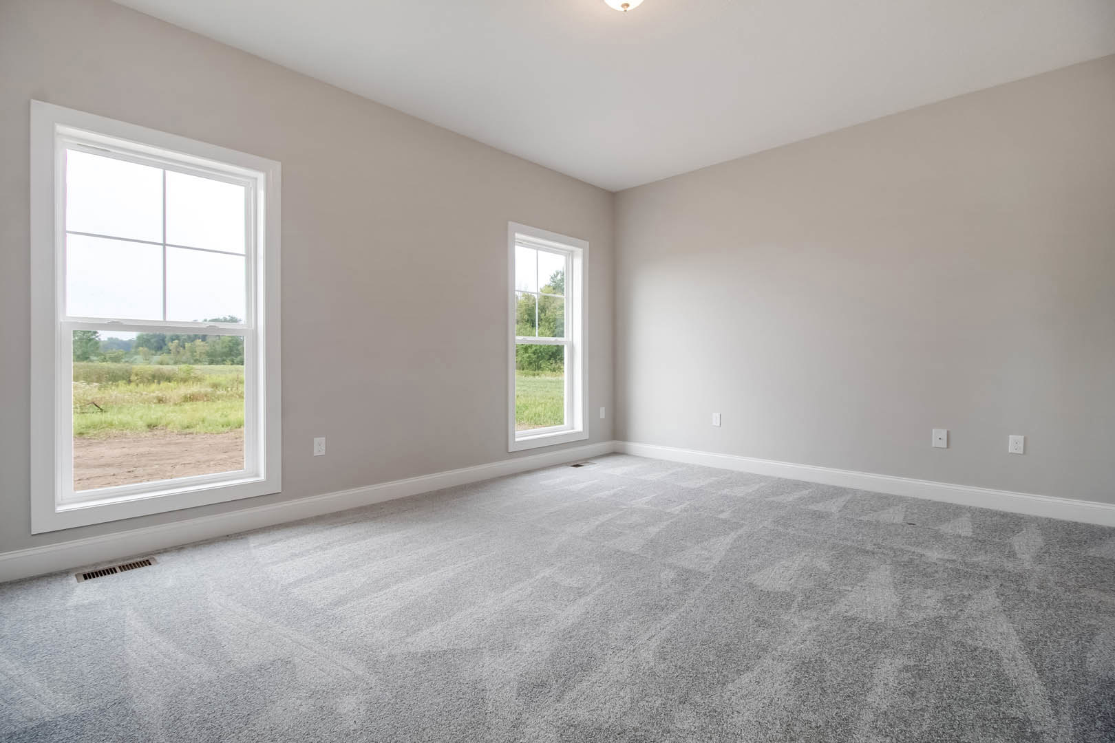 Spacious room with large windows overlooking a field and trees, grey carpet flooring, white ceiling with recessed light fixture