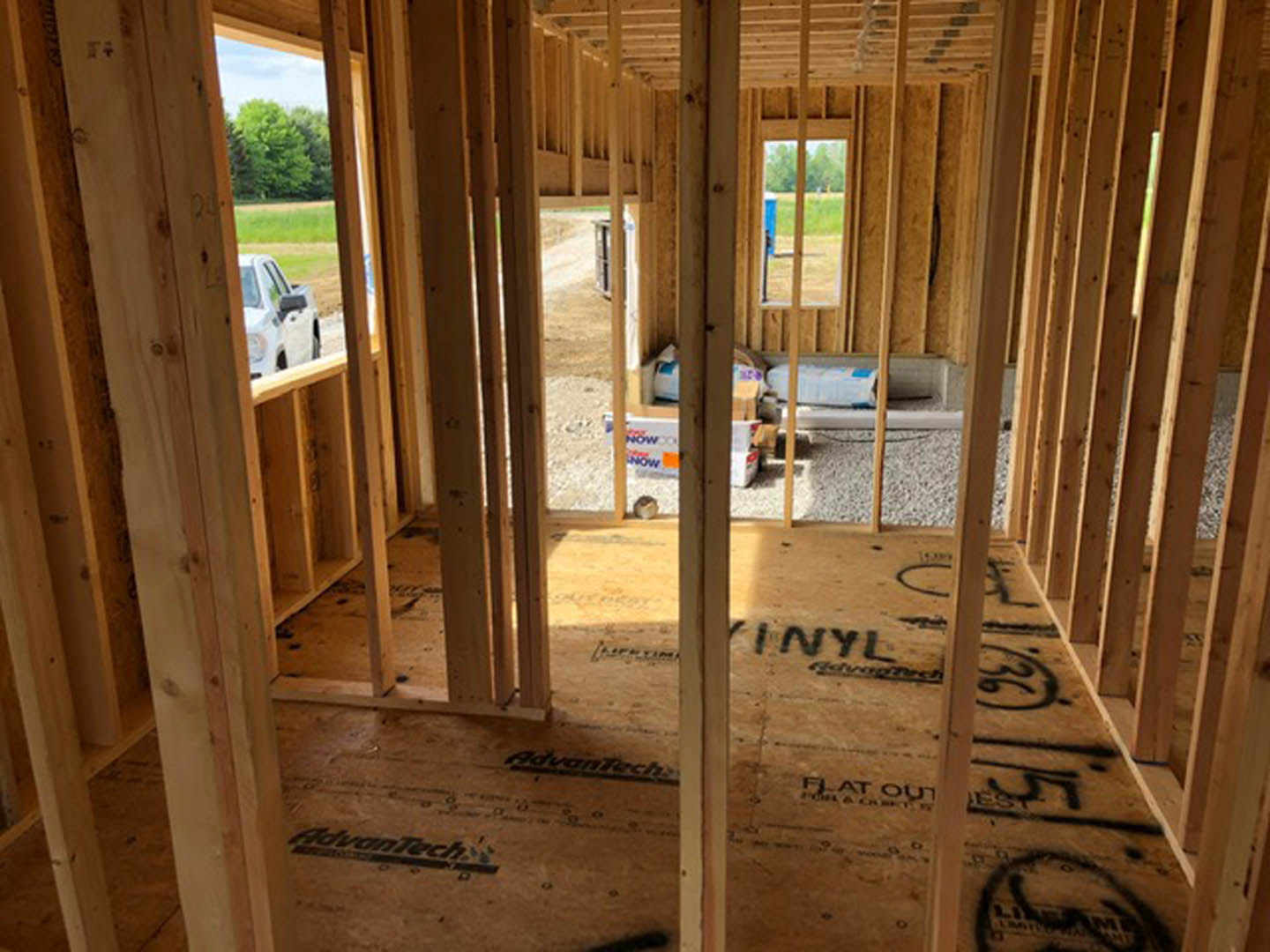 Wood framing and exposed beams inside a partially constructed house, with unfinished floors and windows, and a blurry car visible in the background.