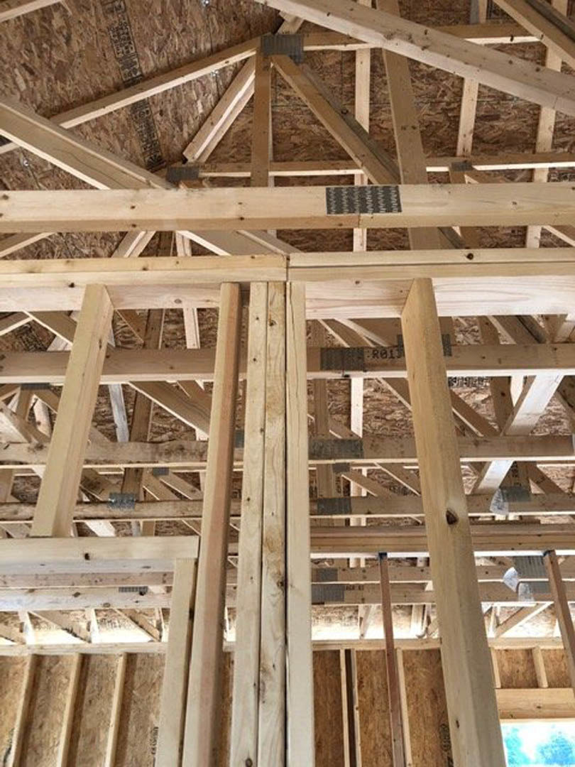 Exposed wooden ceiling beams and plank walls inside a custom home, with natural wood finishes and partial view of a bench against a blurred blue and white sky through windows