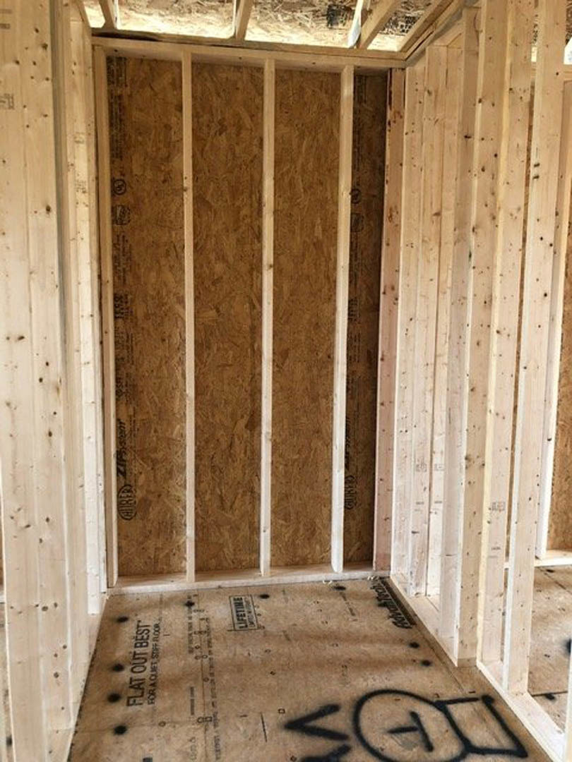Room featuring wood panel walls, plywood flooring, and exposed beams with composite materials visible.
