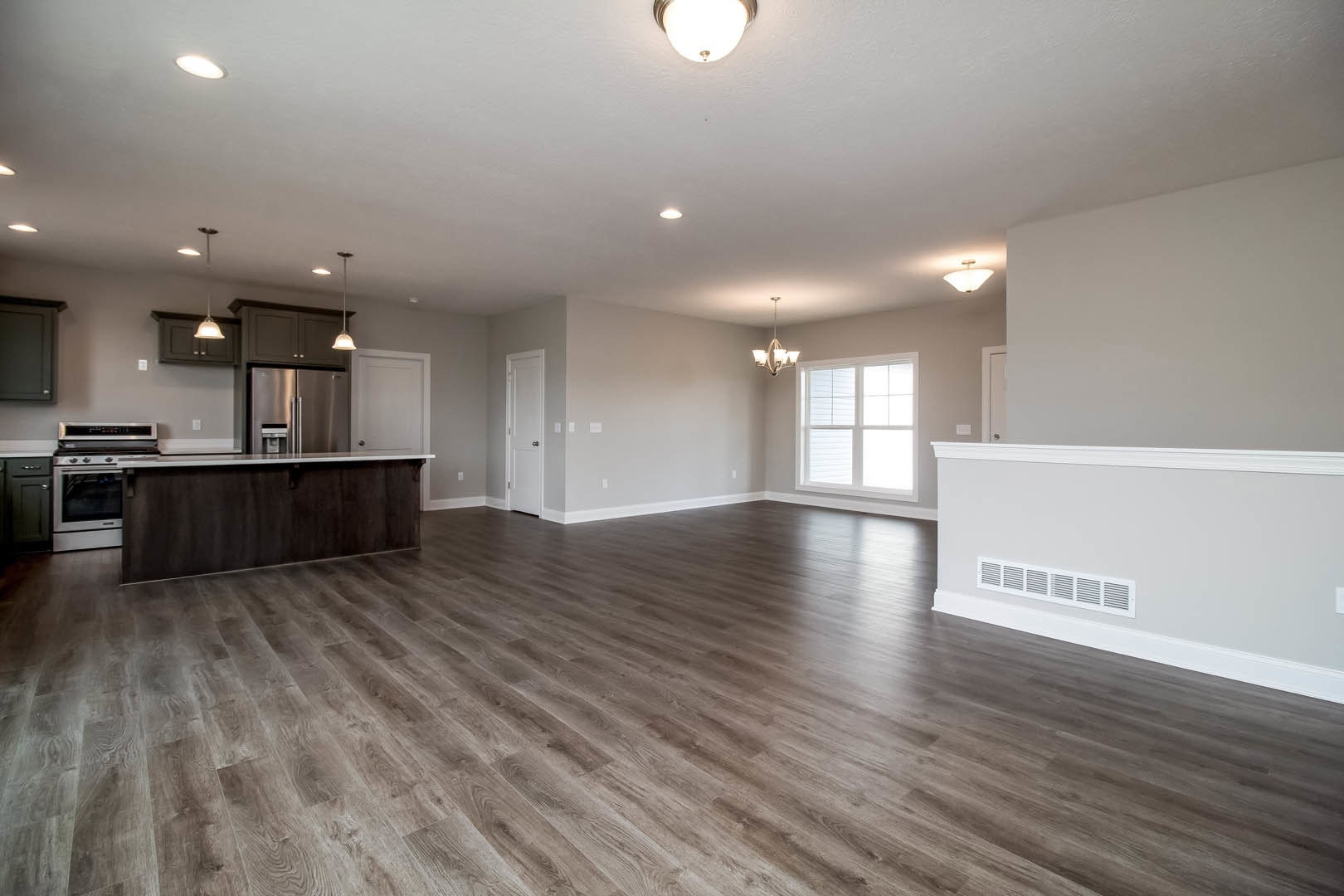 Open kitchen with white countertops, wood cabinetry, stainless steel stove, hardwood flooring, large window, and modern ceiling light fixture