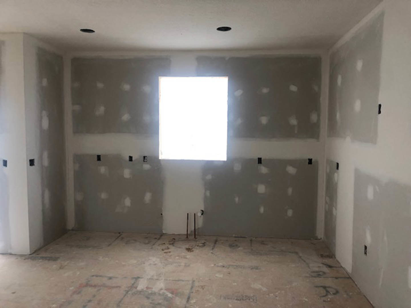 Modern room with plaster walls, square window framed in black, recessed ceiling lights, white baseboard, and light-colored flooring with visible seams.