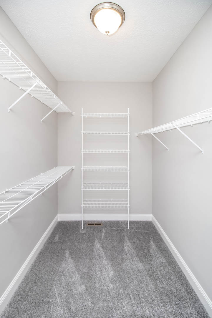 White built-in shelving unit with four shelves mounted on a wall, light fixture on white plaster ceiling, grey carpeted floor, white baseboard molding.