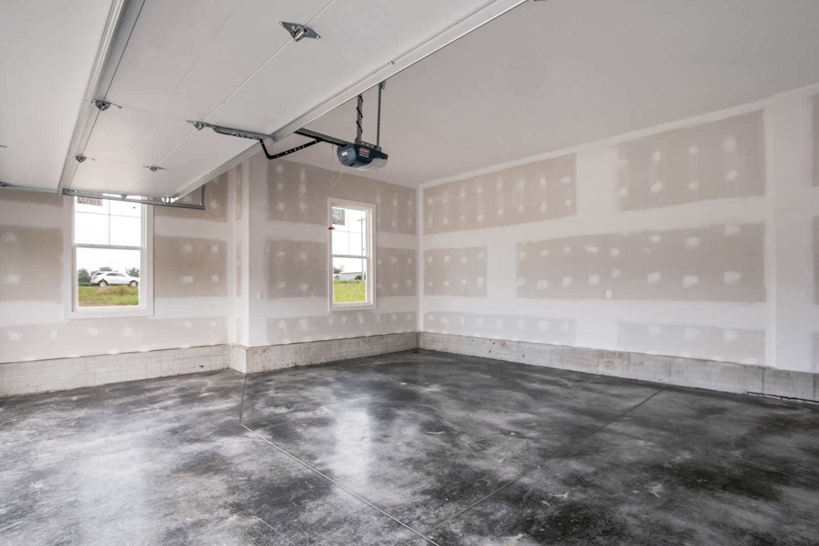 White plaster walls and smooth concrete flooring in a minimalist room with a window and garage door.