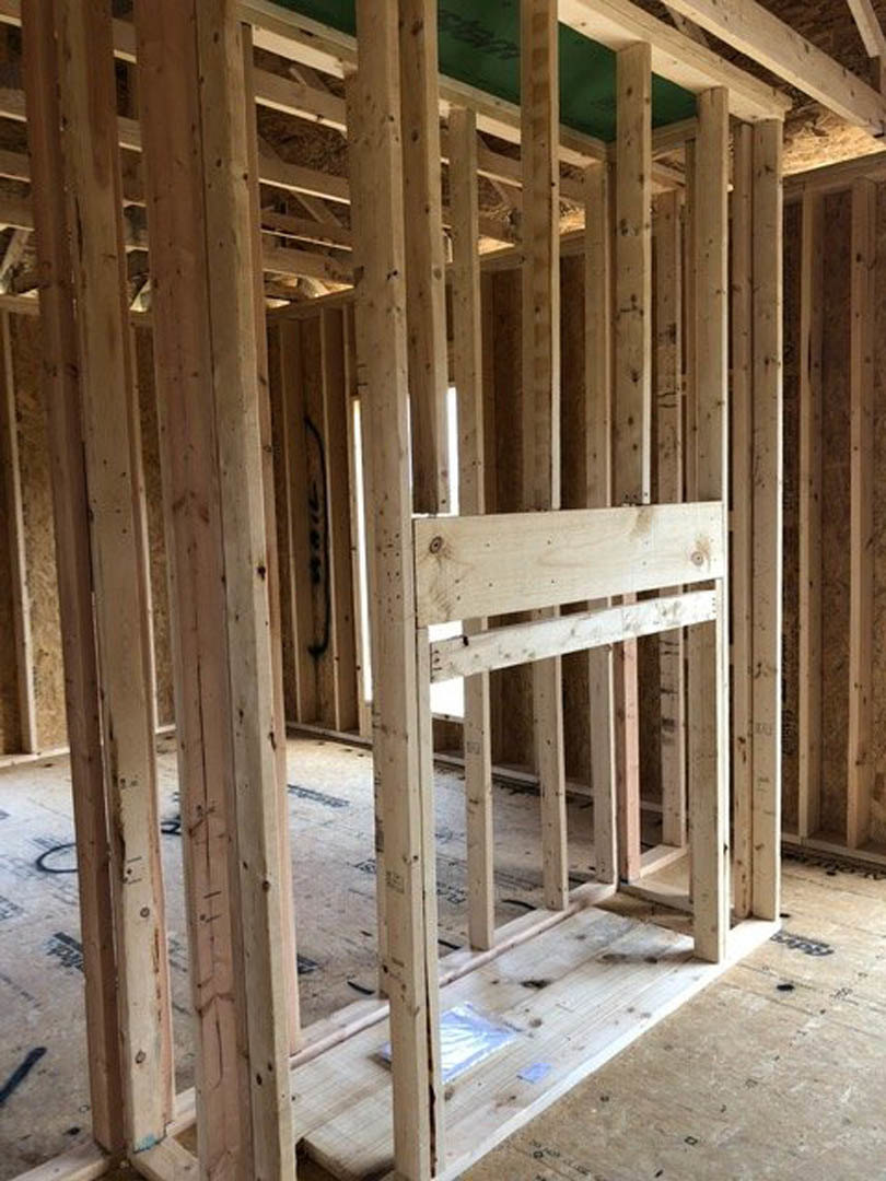 Exposed wood framing with vertical beams, unfinished wooden floor, and visible wall insulation in a residential construction interior