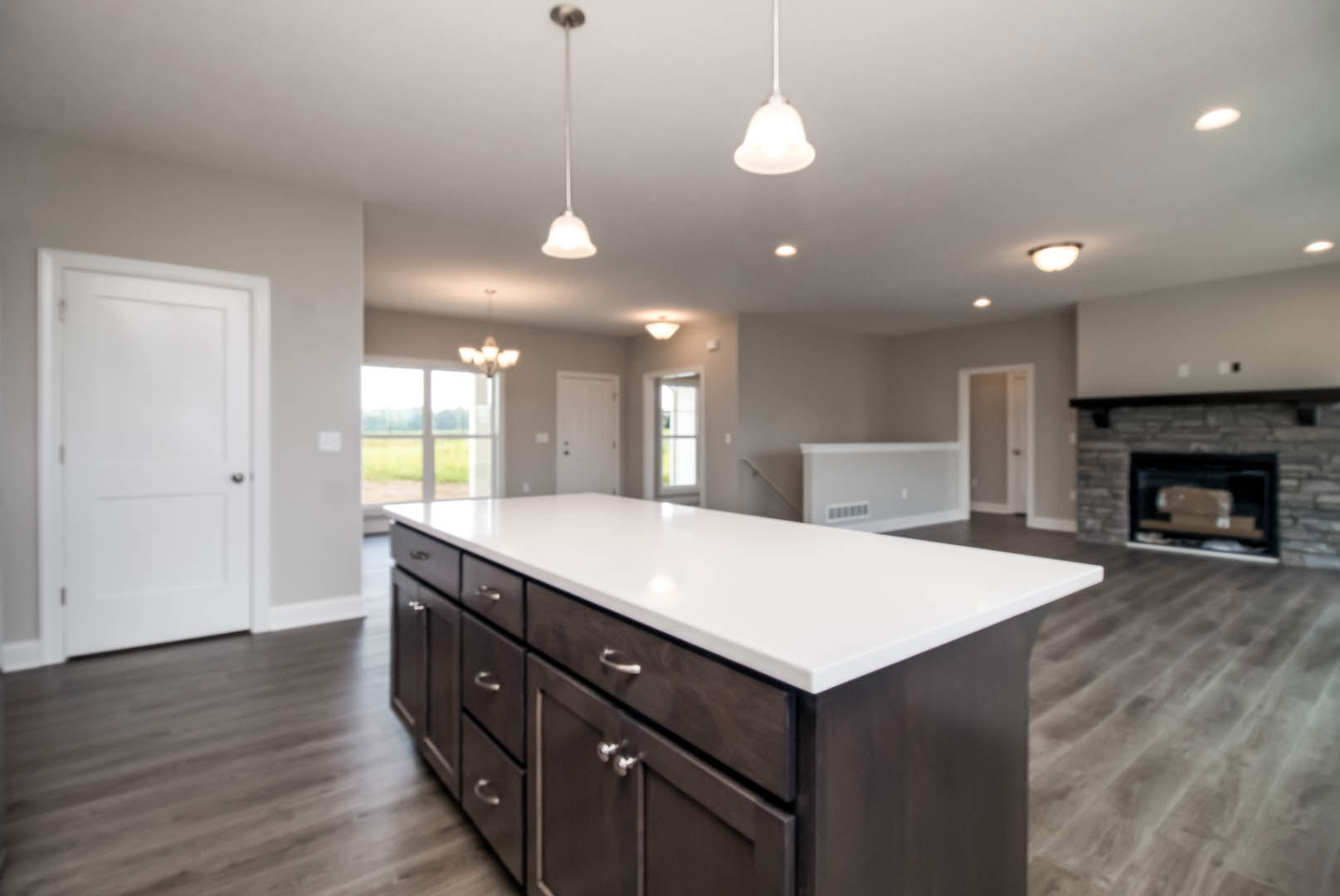 Quartz kitchen island with built-in cabinetry, stainless steel appliances, white door with black handle, hardwood flooring, and modern pendant lighting