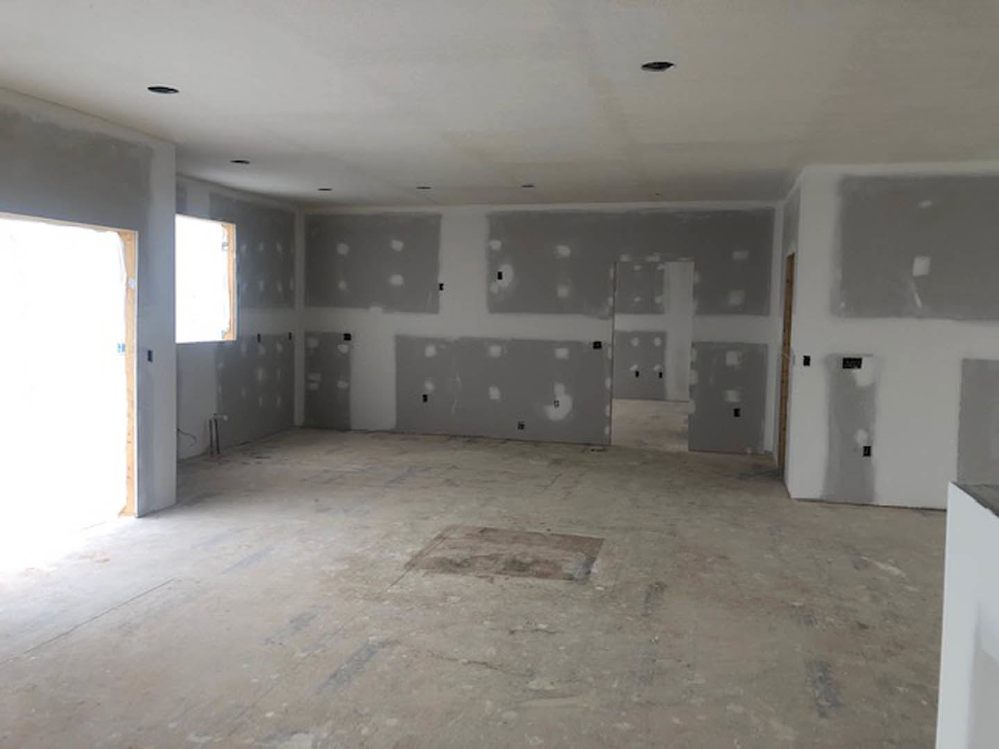 White walls and ceiling, light-colored plaster flooring with a small square object, white door and doorway, close-up of grey surface, blue text visible on a rectangular item.