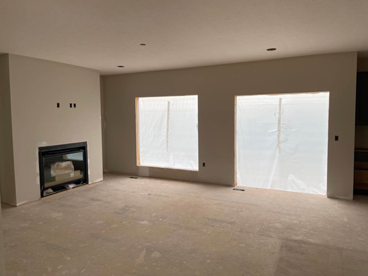 Living room with white plaster walls, large windows, hardwood flooring, and a stone fireplace with a wood mantel