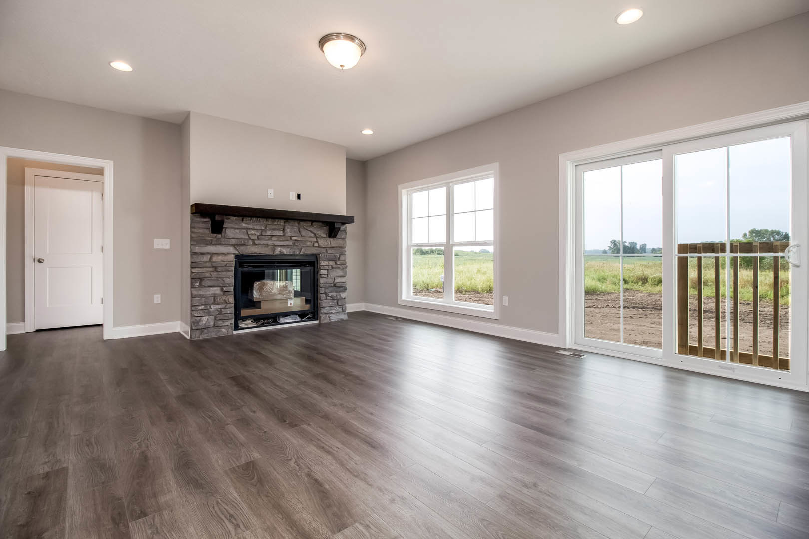 Living room with hardwood floors, white fireplace featuring a glass-enclosed firebox, white door with silver handle, and sliding glass door leading outside