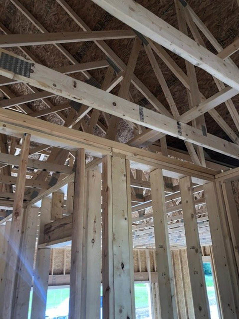 Exposed wooden beams and framing inside a house under construction, with a window revealing greenery outside