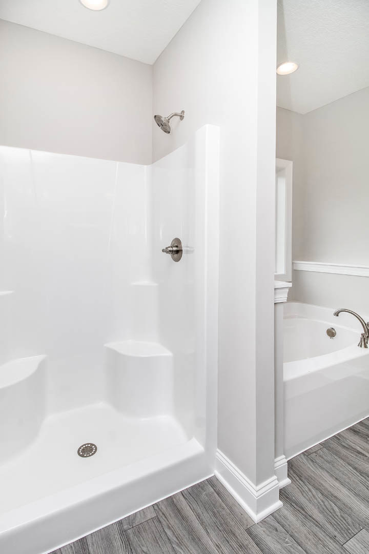 Bathroom featuring white tiled shower with silver handle and drain, adjacent bathtub, chrome faucet and showerhead, neutral walls, and modern plumbing fixtures.