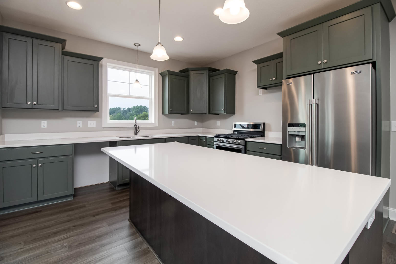 Spacious kitchen featuring a large white island with quartz countertop, stainless steel refrigerator with water dispenser, built-in stove, white cabinetry, and a window allowing
