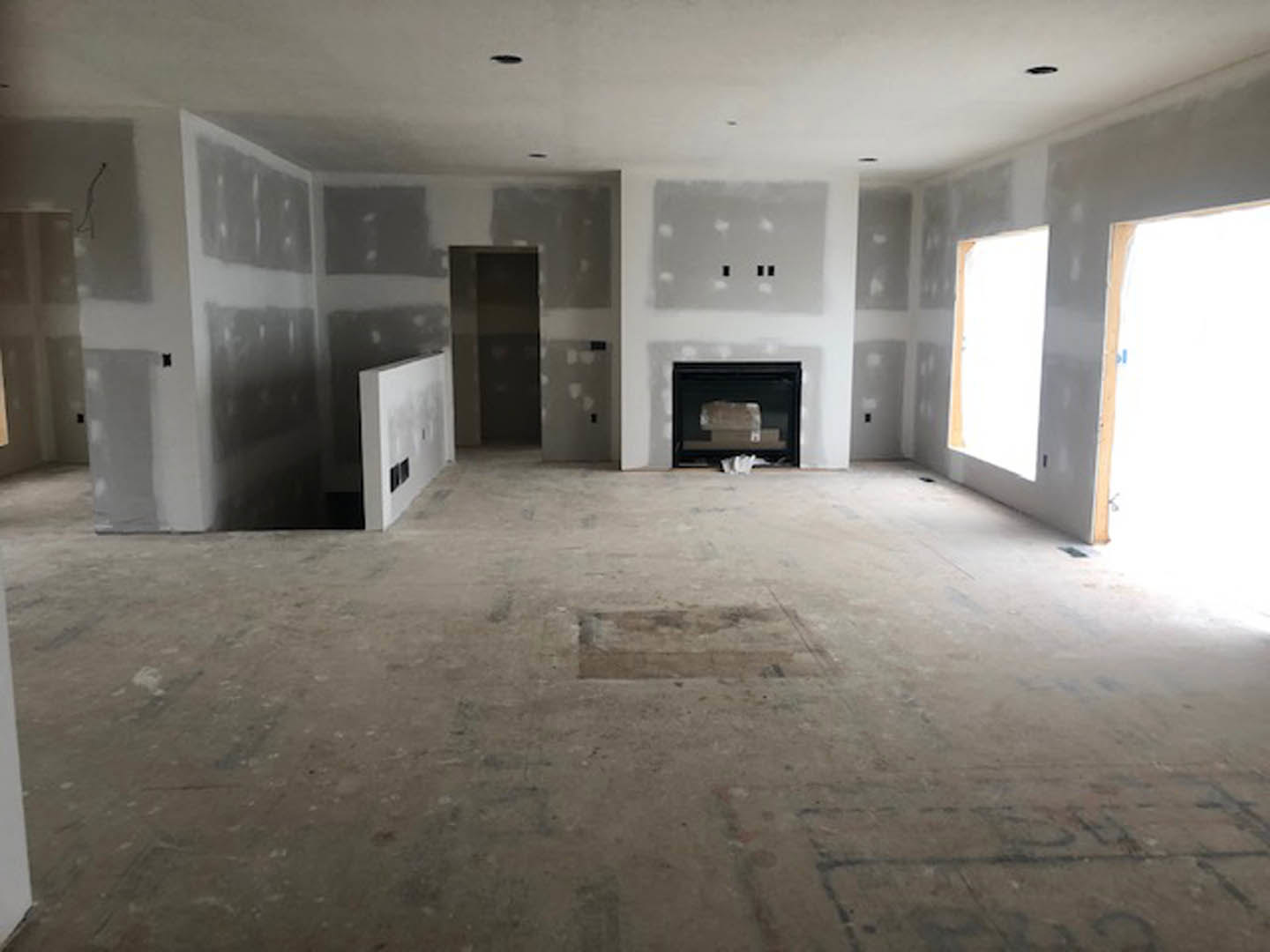 Living room with plaster walls, large windows, black-bordered white accent wall, modern fireplace, concrete flooring, and visible door and television.