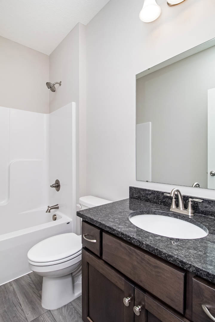 Bathroom with white sink set in black countertop, modern faucet, white toilet, tiled walls, and glass-enclosed shower.