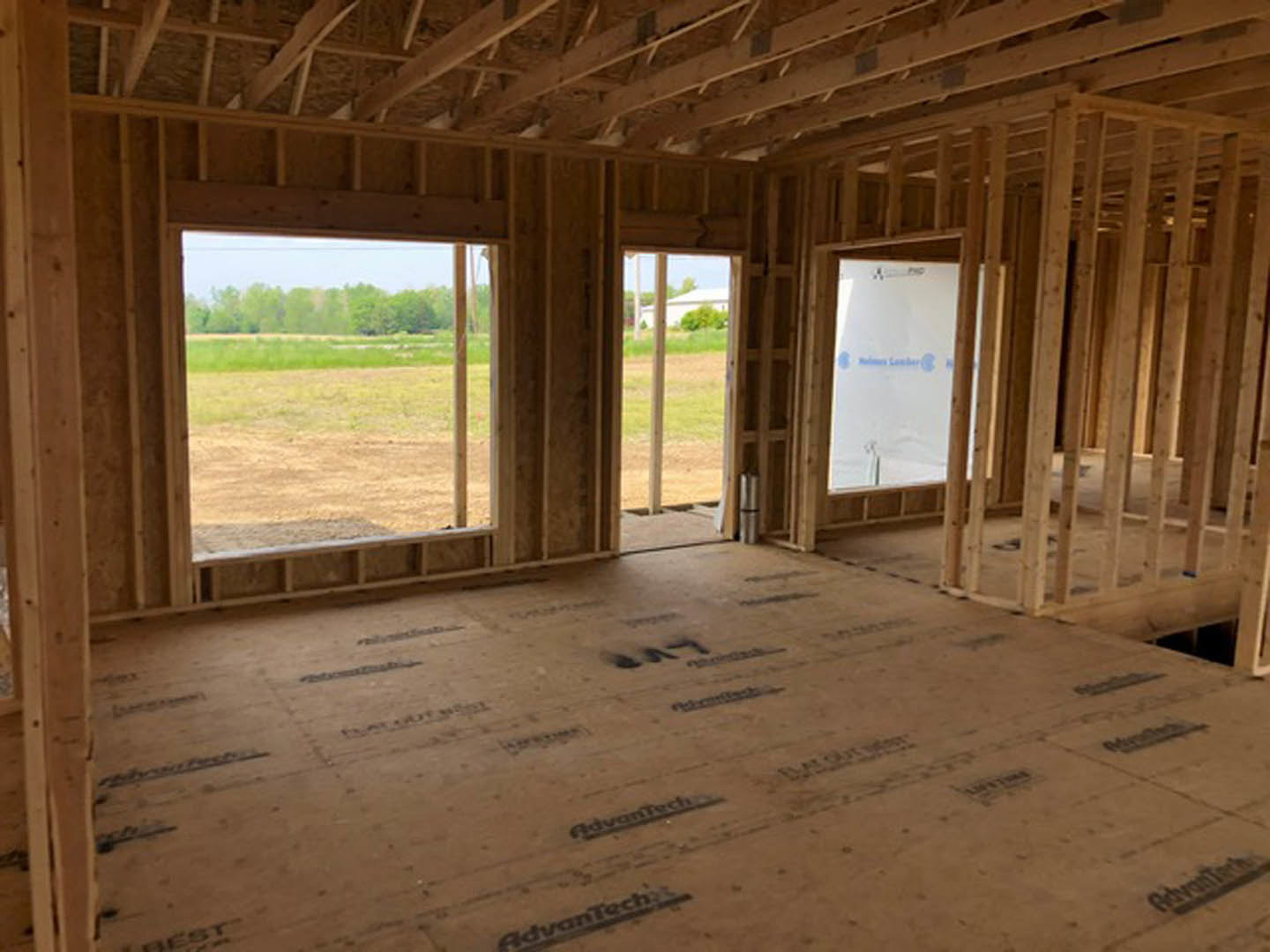 Unfinished room with large windows, exposed wooden beams, and a view of grassy field and trees