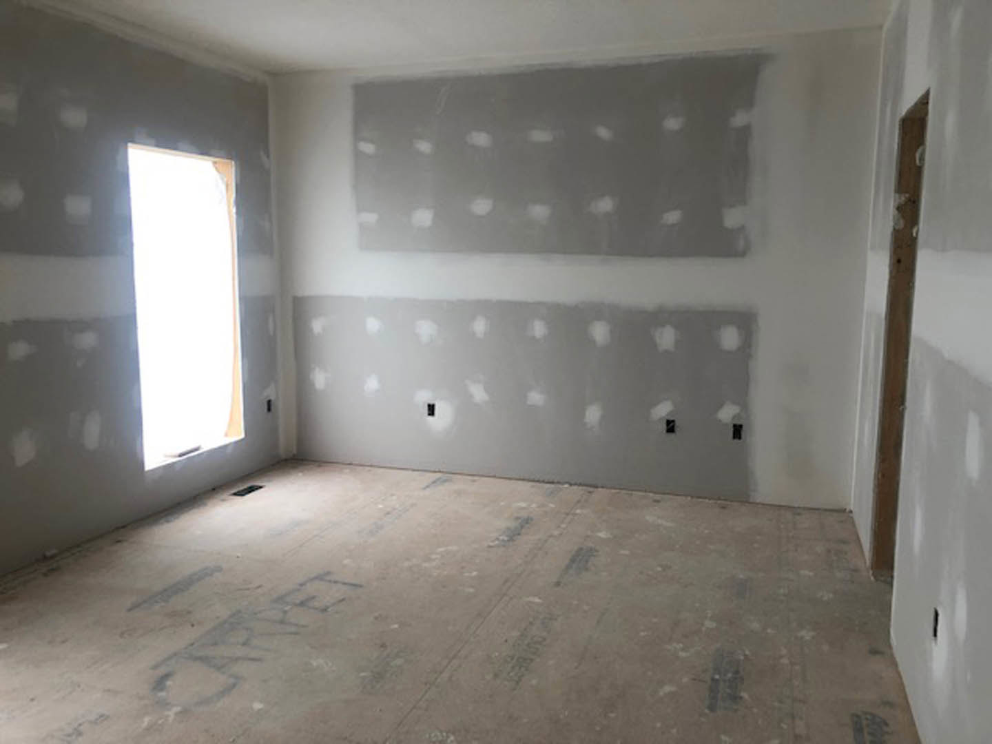 White-walled room with a large window, smooth plaster finish, concrete floor, and ceiling visible.