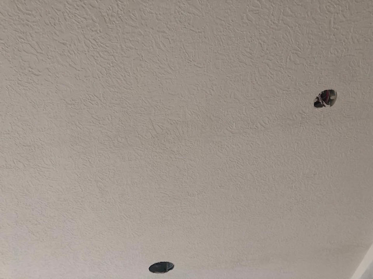 White ceiling with a black object mounted near the center, smooth white surface and recessed lighting visible.