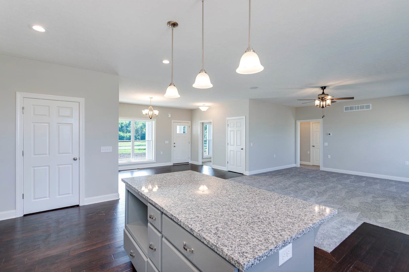 Spacious kitchen featuring marble countertops, white cabinetry, tile backsplash, stainless steel sink, pendant light fixtures, and hardwood flooring