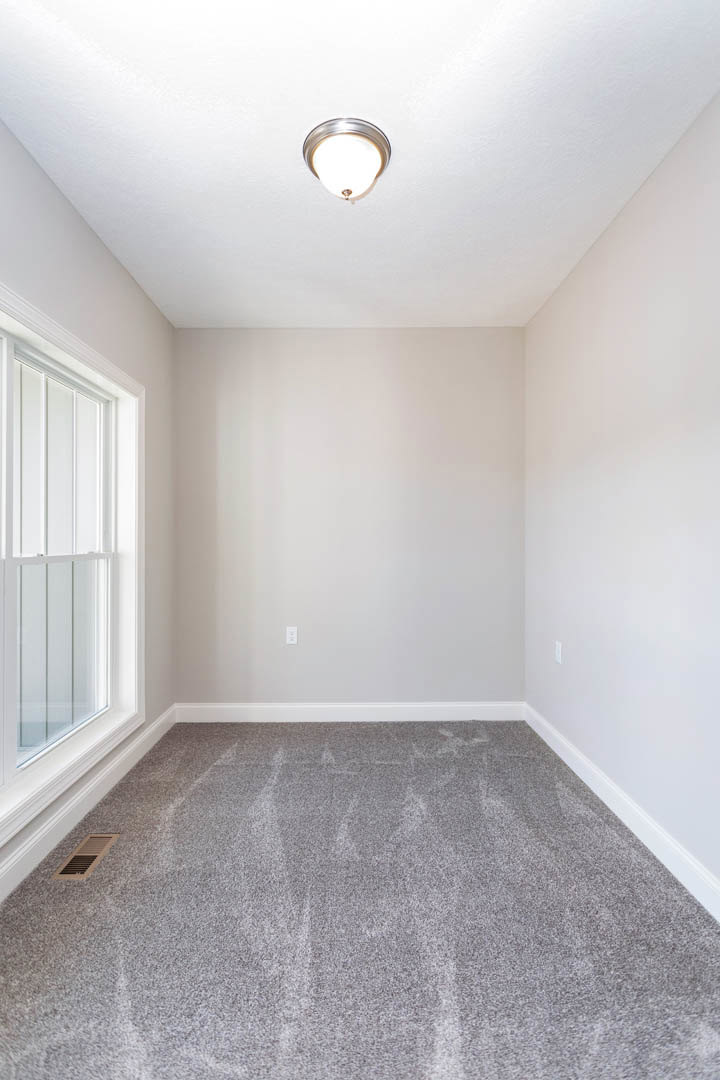 Carpeted room with white walls, ceiling light fixture, window with white trim, and wall vent