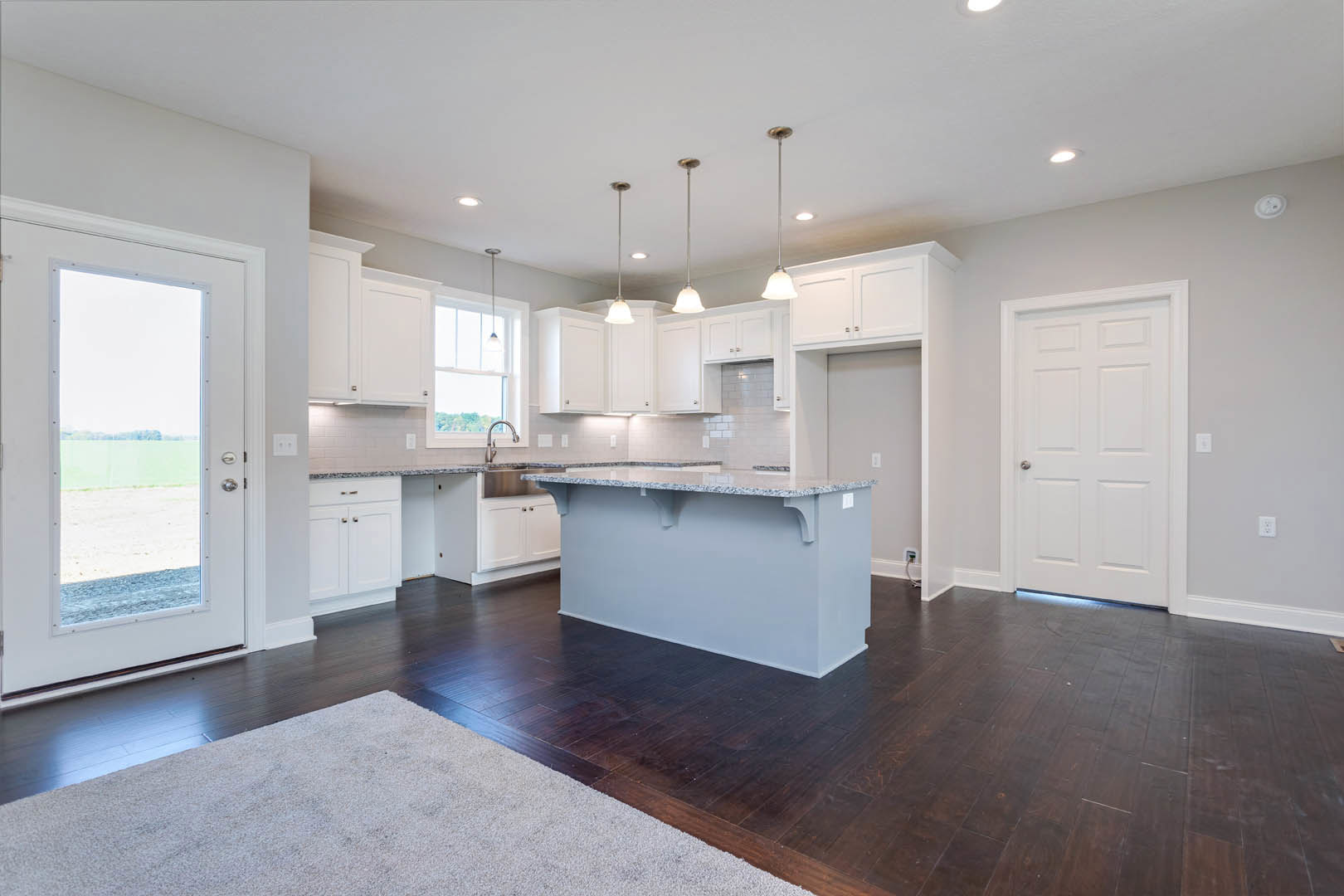 Open kitchen and dining area featuring white cabinetry, marbled countertops, glass door, silver-handled white door, close-up of chrome faucet, and white ceiling with recessed