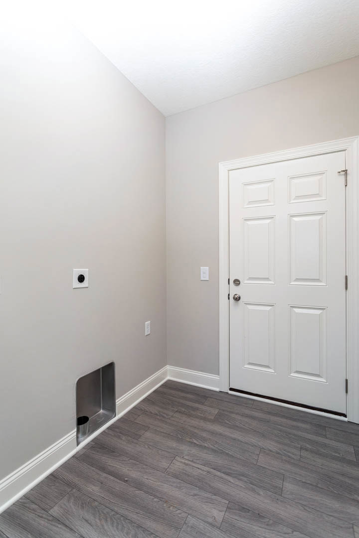 White paneled door with black handle, white frame, and wood laminate flooring with white baseboard trim in a neutral-toned room
