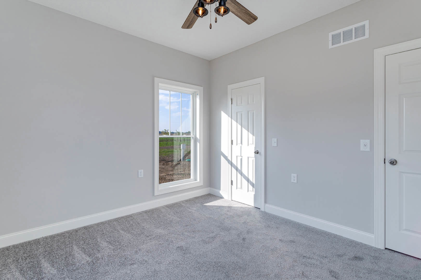 White paneled door with silver knob, large window overlooking grassy field, beige carpet flooring, ceiling fan with light fixture, smooth plaster walls