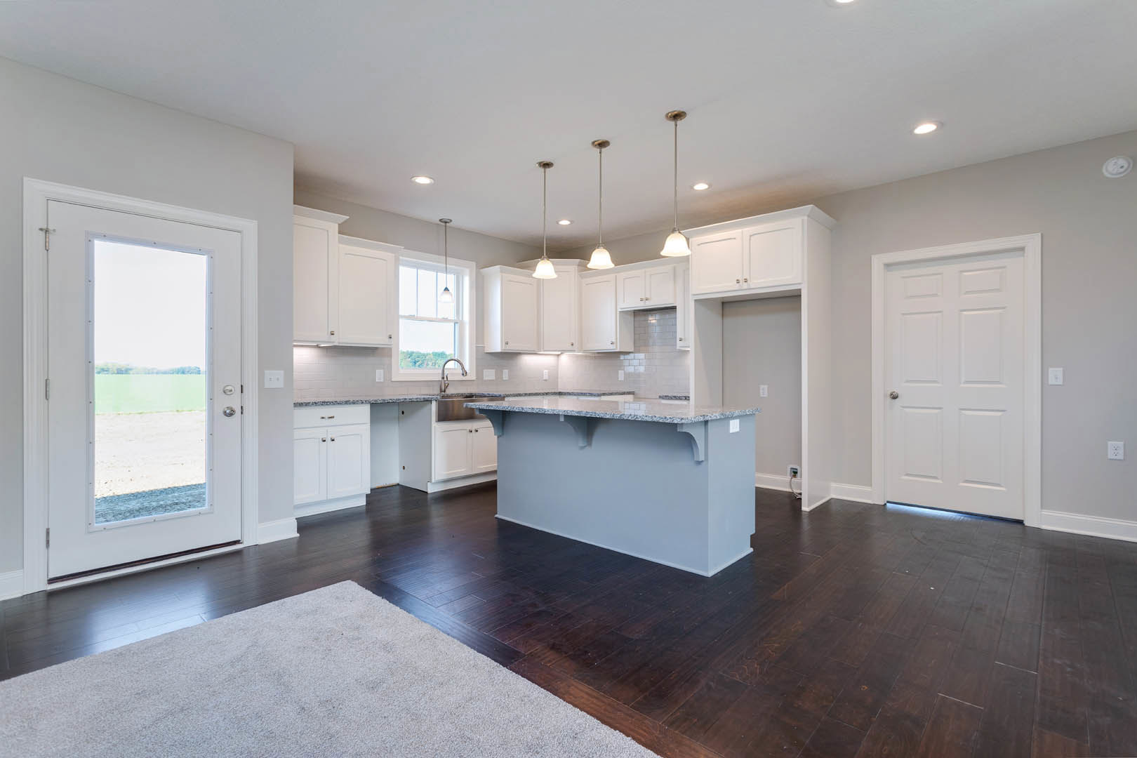 Open kitchen and dining area with light wood flooring, white cabinetry, stone countertop, stainless steel faucet, white door with silver handle, and glass door revealing a field