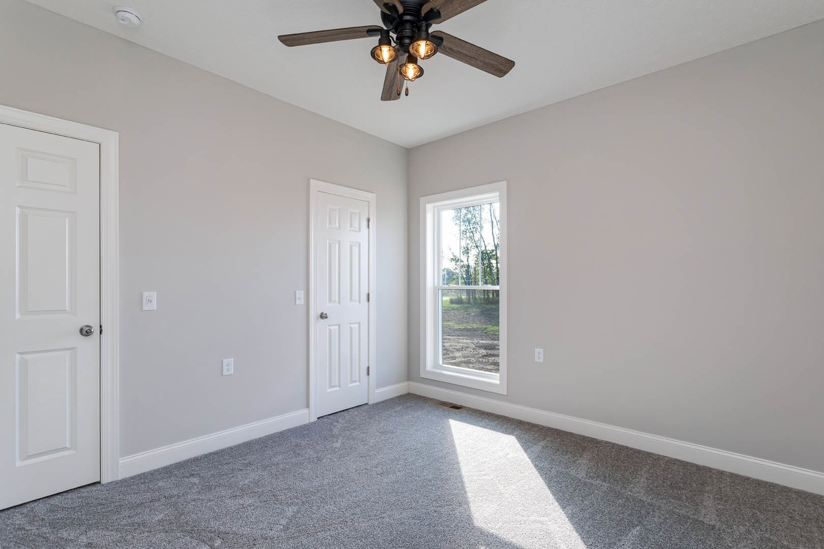 Carpeted room with white door, ceiling fan with lights, window showing trees outside, white walls and baseboard molding