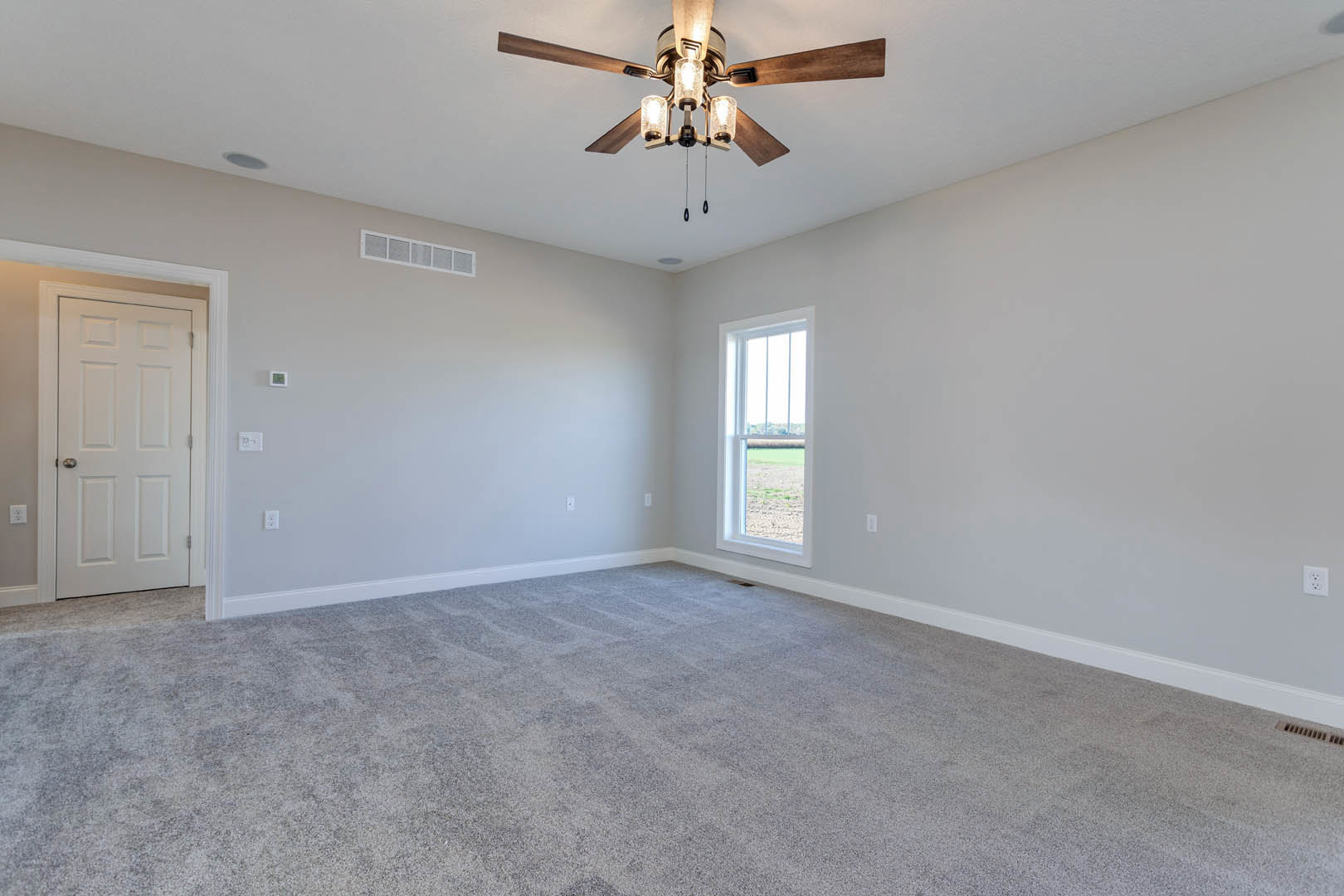 Carpeted room featuring a ceiling fan with lights, white door with silver handle, and square window framed in white overlooking a grassy field