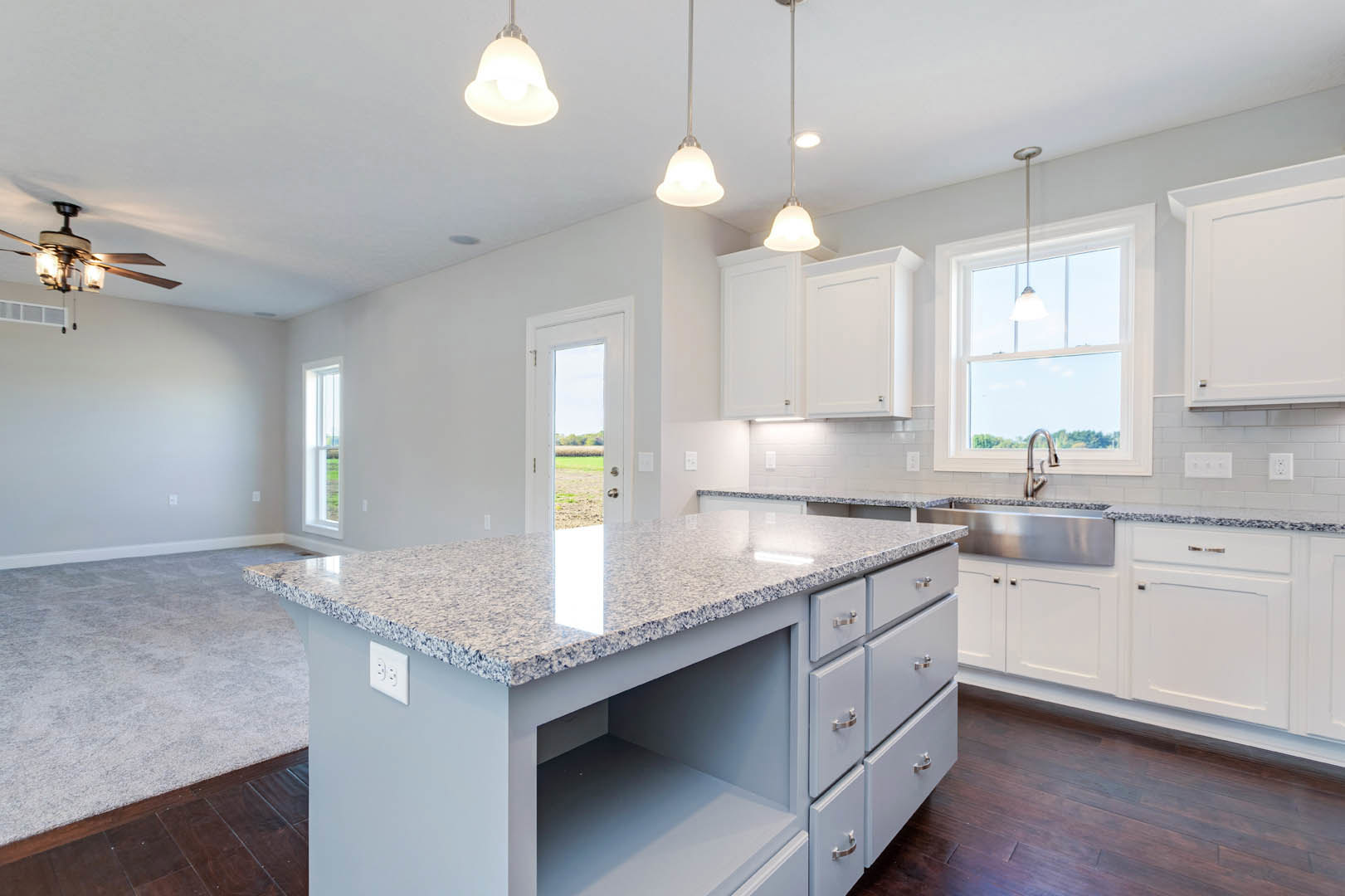 Marble island with waterfall edge, white cabinetry, stainless steel appliances, pendant lights, wide window, hardwood flooring, and granite countertops