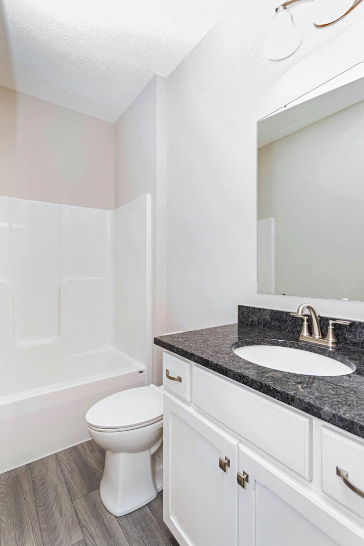 Modern bathroom featuring a white oval sink set on a black countertop, chrome faucet, white toilet, glass-enclosed shower, and light gray tile walls.