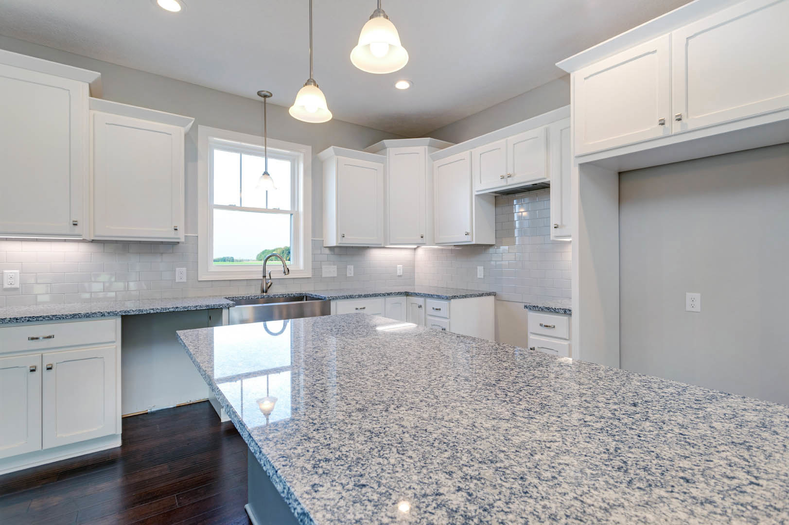 Marble kitchen countertop with white cabinetry, stainless steel sink, tile backsplash, ceiling light fixture, and window.