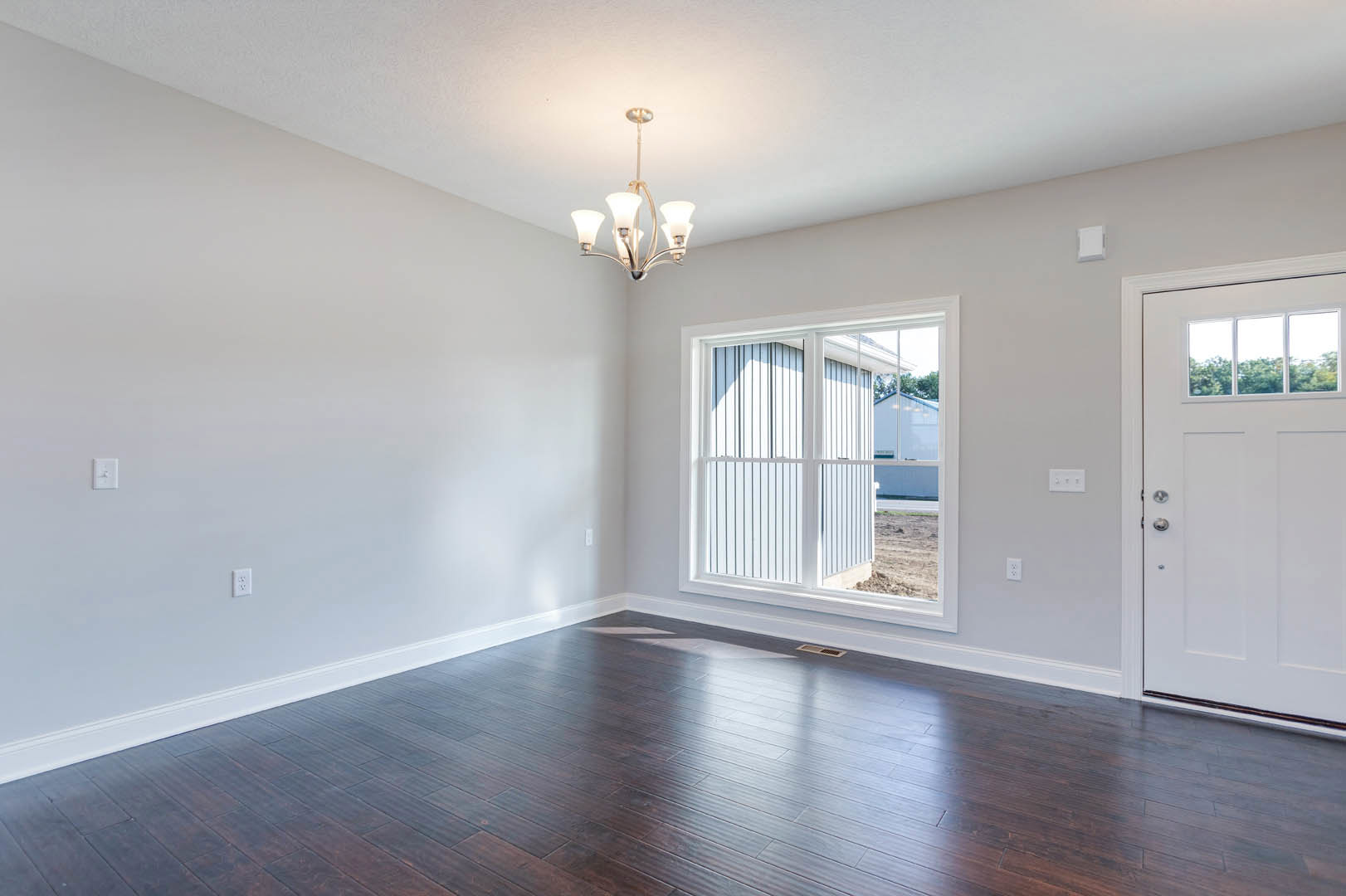 Room with dark hardwood flooring, white walls, white door with glass window, white-framed window showing trees outside, close-up of chandelier, plaster molding along ceiling.