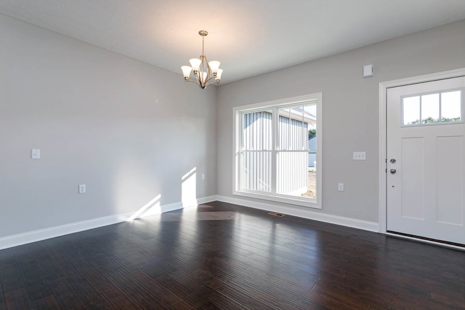 Dark wood flooring, white walls with crown molding, large window, white door with glass panel, ornate chandelier hanging from ceiling.