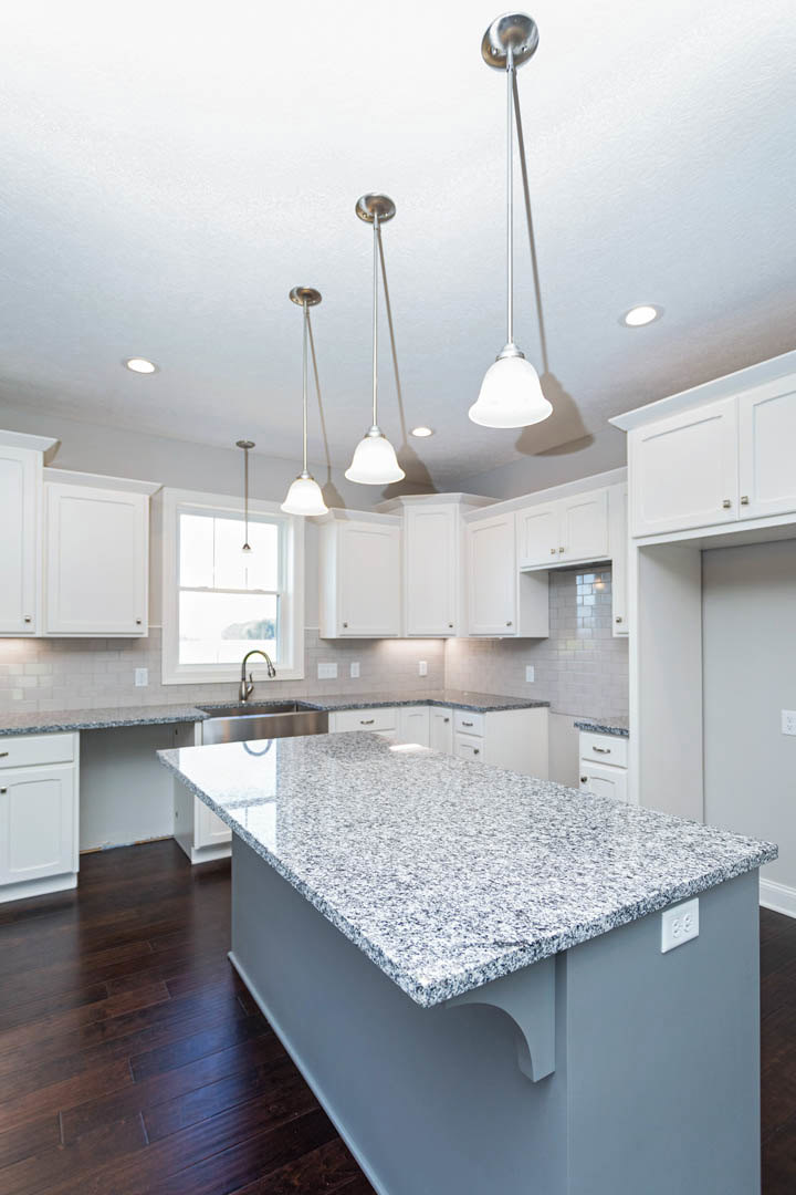 Granite kitchen island with stainless steel sink, white cabinetry with silver handles, light streaming through window, modern appliances and neutral walls
