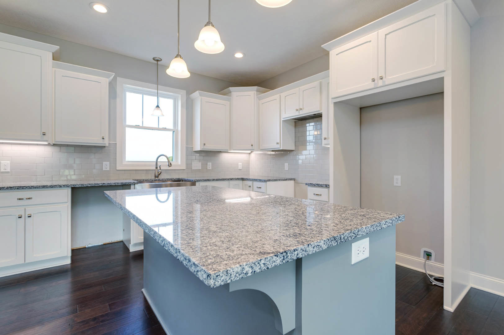 Granite island with white cabinets and countertops, stainless steel sink, tile backsplash, ceiling lights, and built-in outlets in a modern kitchen.