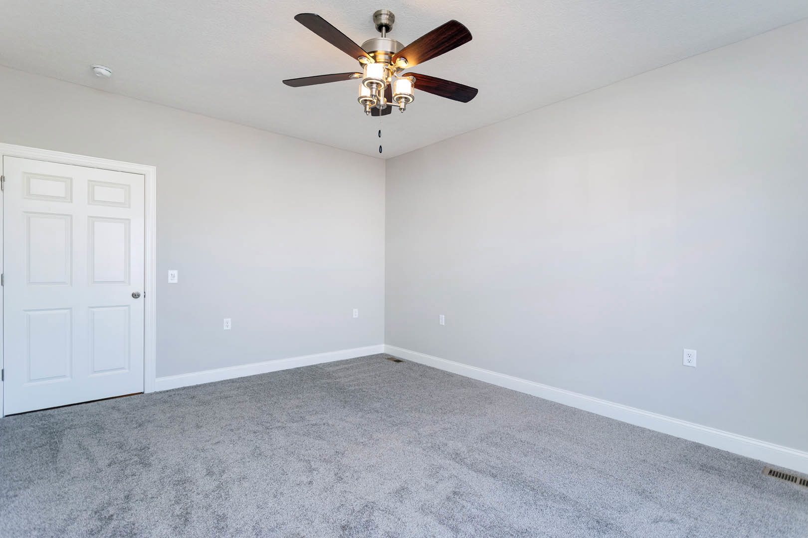Ceiling fan with lights mounted on white ceiling, grey carpeted floor, white door with silver handle and white door frame, neutral walls, simple molding